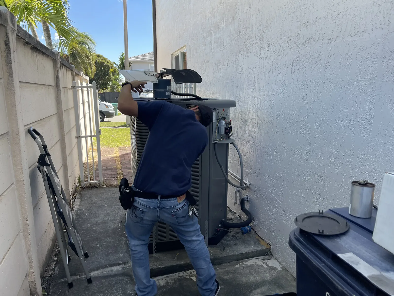 A Dade Super Cool technician lifting the fan assembly from an outdoor condenser during a scheduled maintenance visit